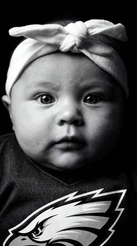 Black and white close-up portrait of a baby wearing a bow headband and football jersey