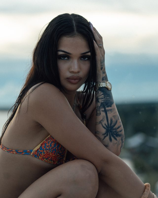 Close-up portrait of a tattooed woman in a patterned bikini seated by the water