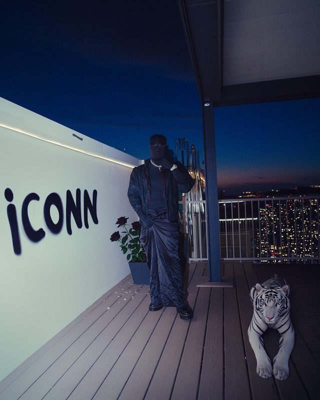 Man dressed in black standing beside a white tiger on a rooftop at night