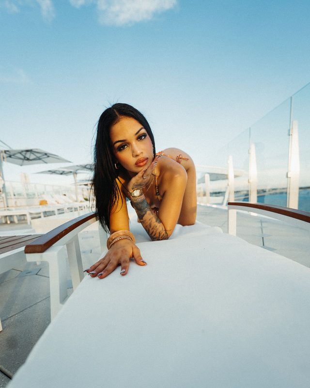 Dark-haired woman in a patterned bikini leaning on a white poolside daybed at sunset